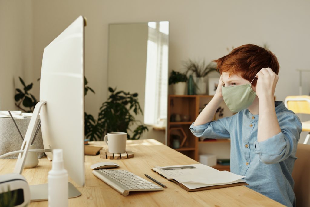 A boy in a mask looks at a computer