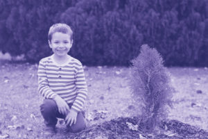 A boy smiles beside a plant
