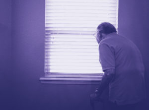 An older man with a walker looks out a window